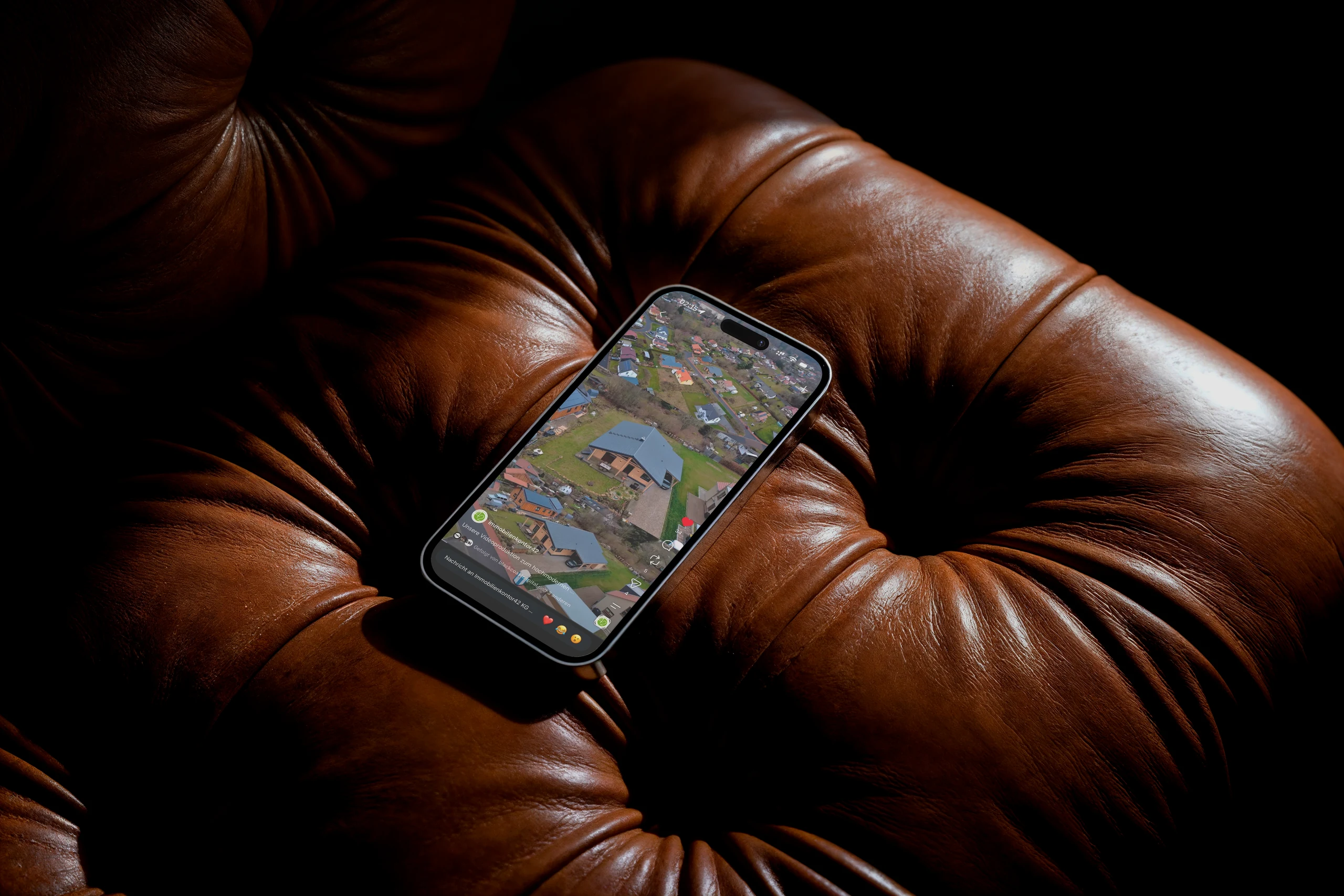 Smartphone auf einem braunen Ledersessel mit einer Luftaufnahme einer Wohnsiedlung im Instagram-Auftritt von Immobilienkontor42
