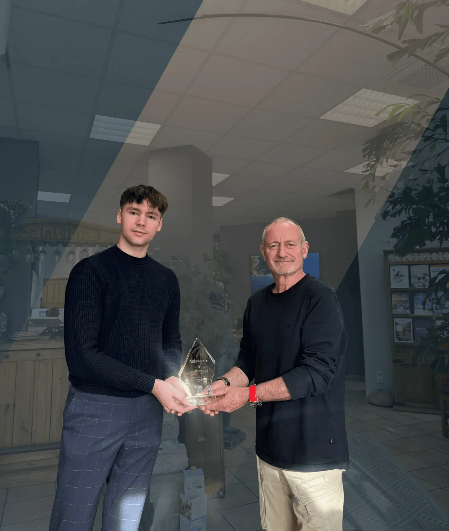 Zwei Männer halten gemeinsam eine gläserne Trophäe in einem Büro